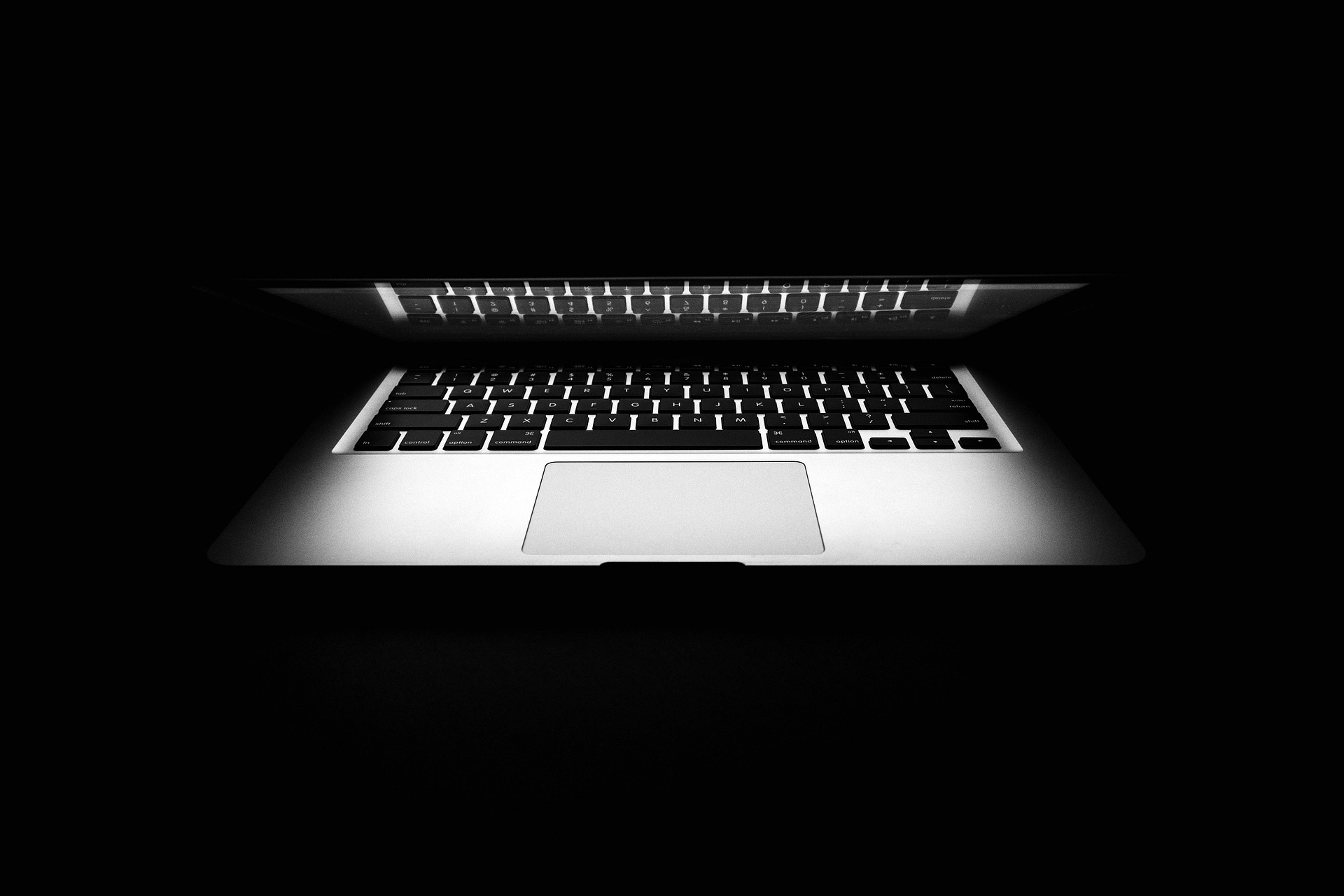 Black and white close-up of a backlit laptop keyboard and trackpad against a dark background